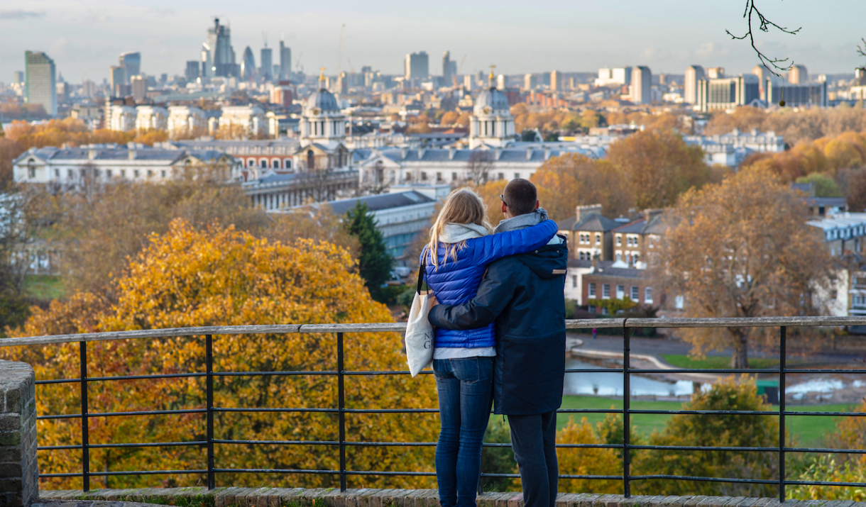 A couple stand at the Queen Elizabeth Oak in Greenwich Park and look out over Greenwich.